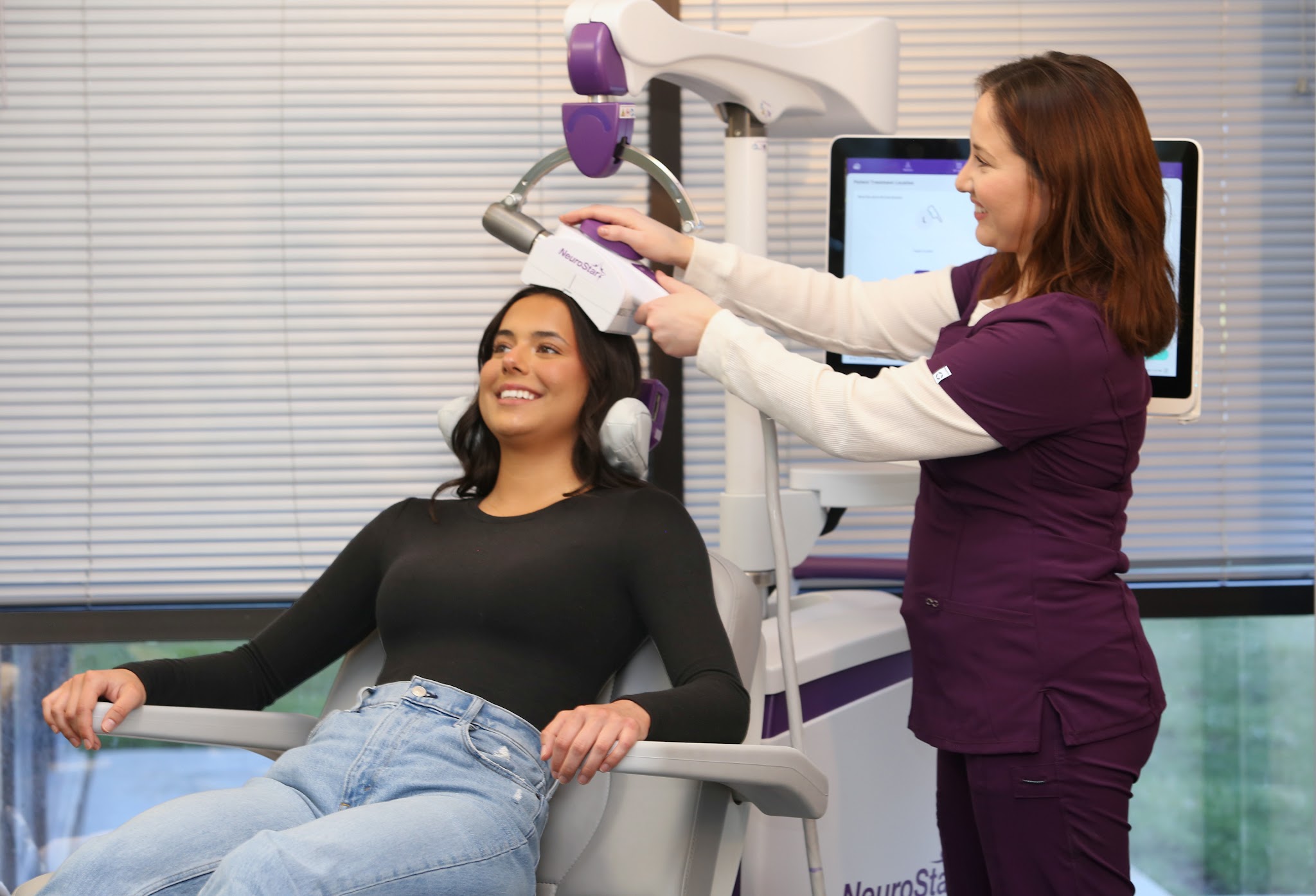 Patient sits comfortably while a clinician positions a NeuroStar magnetic coil against her scalp.